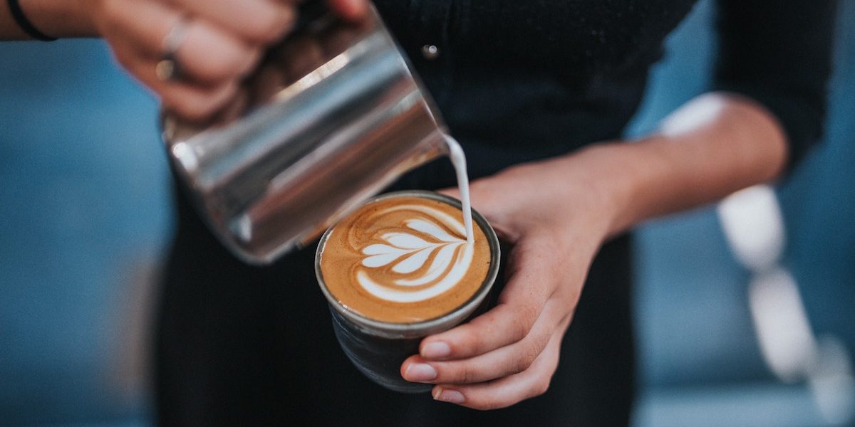 A close-up shot on a barista pouring milk into a cup of coffee to create latte art