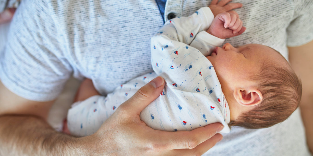 Newborn baby sleeping on father’s chest while he’s on parental leave